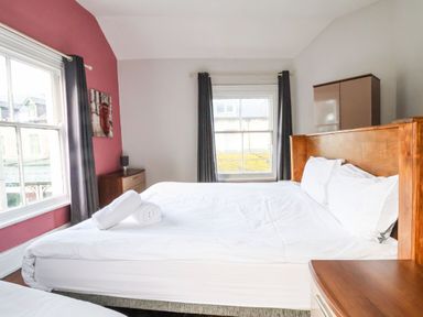 A bedroom with a large bed with white linens two windows with curtains a wooden headboard and furniture at Mountain View in Penmaenmawr