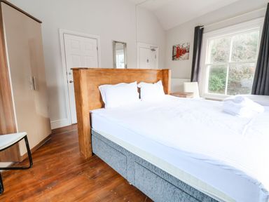 A bedroom with a double bed wooden headboard white bedding wardrobe chair and window at Mountain View in Penmaenmawr