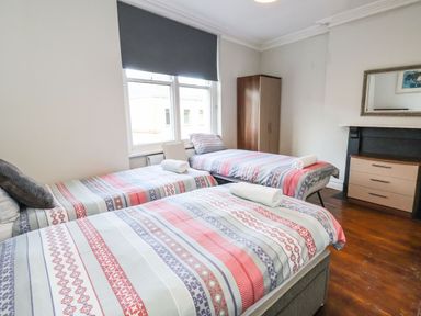 A bedroom with three single beds a wardrobe a chest of drawers and a window with a blind at Mountain View Penmaenmawr