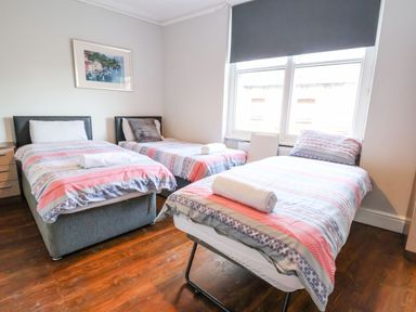 A bedroom with three single beds with rolled towels on each a window with a blind and a wooden floor at Mountain View in Penmaenmawr