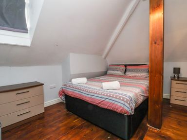 A bedroom with a double bed between two dressers with lamps and a wooden beam in Mountain View in Penmaenmawr