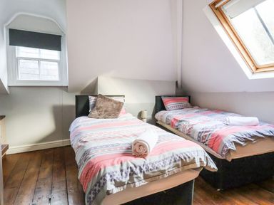 A bedroom with two single beds with patterned bedspreads and pillows by windows at Mountain View in Penmaenmawr