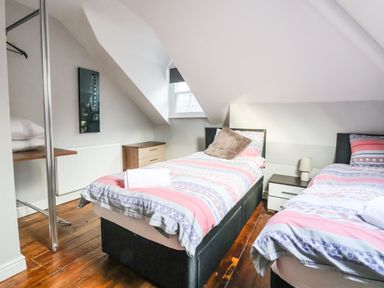 A bedroom with two single beds a nightstand with a lamp a window and a small dresser at Mountain View in Penmaenmawr