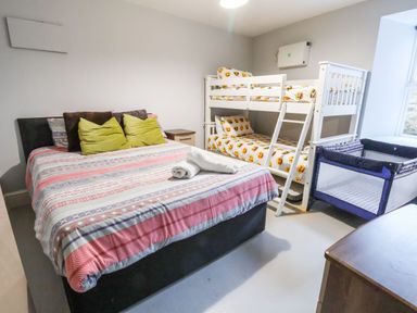 A bedroom with a double bed, bunk beds with emoji bedding, a crib, and a window at Mountain View in Penmaenmawr