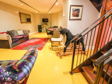 A room with a patchwork sofa a multicolor couch a red and gray rug a poker table with chairs a rocking horse and wooden stairs at Mountain View in Penmaenmawr