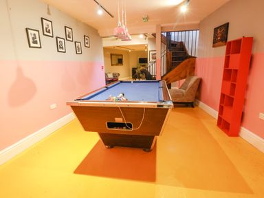 A room with a pool table blue felt red bookshelf beige chair and staircase at Mountain View in Penmaenmawr