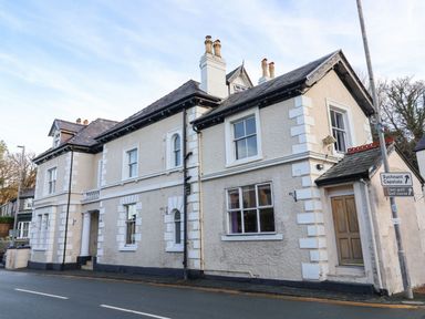 A street view of a two story building with white textured walls and multiple chimneys at Mountain View in Penmaenmawr