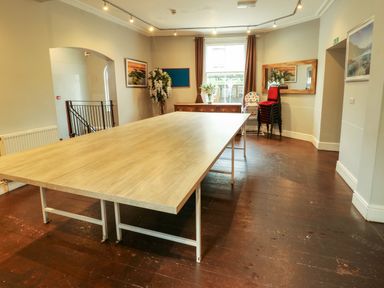 A room with a large wooden table in the center a stack of red chairs a high chair a wooden dresser with flowers and a window behind it at Mountain View in Penmaenmawr