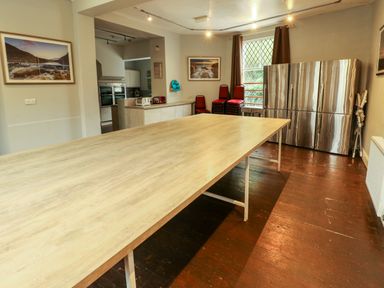 A room with a large wooden table in the center stainless steel refrigerators stacked chairs and kitchen appliances at Mountain View in Penmaenmawr