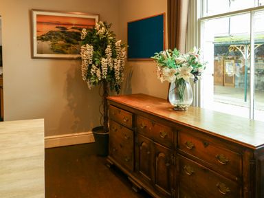 A wooden sideboard with a vase of flowers on top next to a potted plant and a window in a room at Mountain View Penmaenmawr