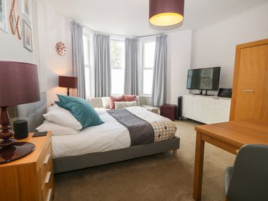 A bedroom with a bed a sofa a wooden table a TV cabinet and a window with curtains at Y Castell Apartment 1 in Criccieth
