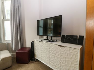 A television on a white cabinet next to a window with gray curtains in a room at Y Castell Apartment 1 in Criccieth