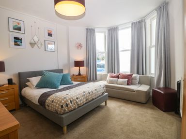 A bedroom with a bed, sofa, bedside tables, lamps, and framed pictures at Y Castell Apartment 1 in Criccieth