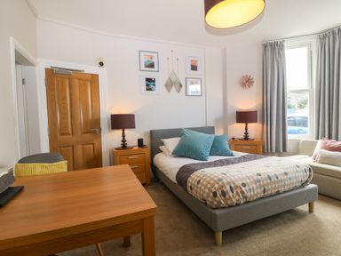A bedroom with a bed sofa wooden table two bedside tables with lamps and wall art at Y Castell Apartment 1 in Criccieth