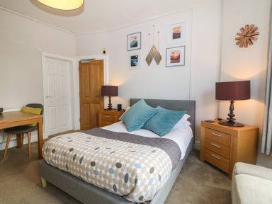 A bedroom with a double bed two bedside tables with lamps a wooden table and chair and framed pictures on the wall at Y Castell Apartment 1 in Criccieth