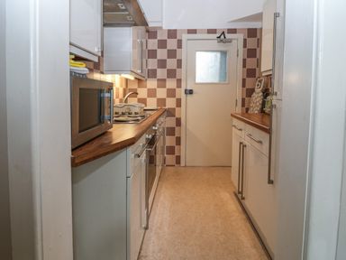A galley kitchen with wood countertops a microwave oven and checkered tile backsplash at Y Castell Apartment 1 in Criccieth