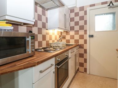 A kitchen with a microwave oven stovetop sink and a door at Y Castell Apartment 1 in Criccieth