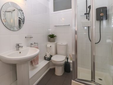A bathroom with a pedestal sink toilet glass-enclosed shower and a round mirror at Y Castell Apartment 1 in Criccieth