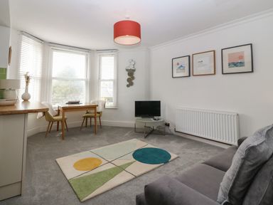 A living room with a gray sofa a small TV on a round table a rectangular dining table with two chairs and a geometric rug at Y Castell Apartment 2 in Criccieth