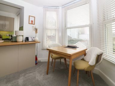 A dining area with a wooden table and two chairs next to windows with blinds at Y Castell Apartment 2 in Criccieth