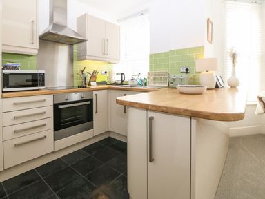 A kitchen with white cabinets green tiled backsplash wooden countertops and various appliances at Y Castell Apartment 2 in Criccieth