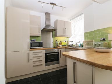 A kitchen with beige cabinets wooden countertops green tiled backsplash and appliances at Y Castell Apartment 2 in Criccieth