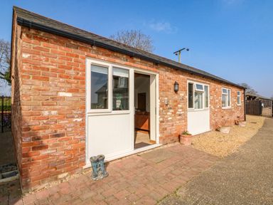 A brick exterior of a house with white doors and windows and a pair of boots outside at Sunnyside Cottage in Blackborough End near King's Lynn