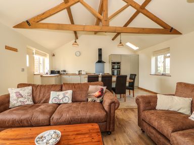 An open living room and kitchen with brown sofas and wooden beams at Sunnyside Cottage in Blackborough End near Kings Lynn