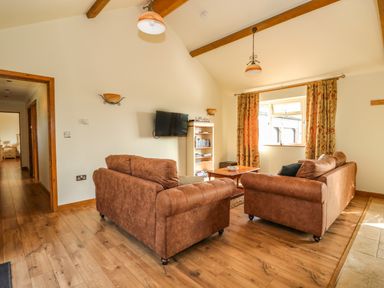 A living room with two brown sofas a wooden coffee table a wall-mounted TV and a bookshelf at Sunnyside Cottage in Blackborough End near Kings Lynn