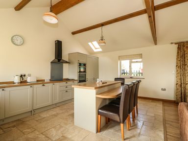 A kitchen with an island and three chairs under wooden beams at Sunnyside Cottage in Blackborough End near Kings Lynn