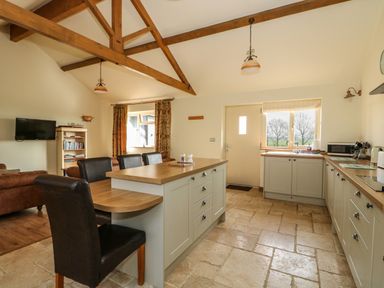 A kitchen with an island and chairs next to a living area with sofas and a TV at Sunnyside Cottage in Blackborough End near King's Lynn
