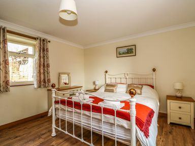 A bedroom with a white metal bed frame red throw pillows and bedside cabinets at Sunnyside Cottage in Blackborough End near Kings Lynn