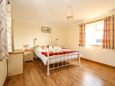 A bedroom with a double bed white frame with bedside tables and lamps wooden floor and floral curtains at Sunnyside Cottage in Blackborough End near King's Lynn