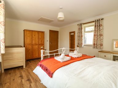 A bedroom with a white metal bed with orange throw and folded towels wooden wardrobe and crib at Sunnyside Cottage in Blackborough End near Kings Lynn