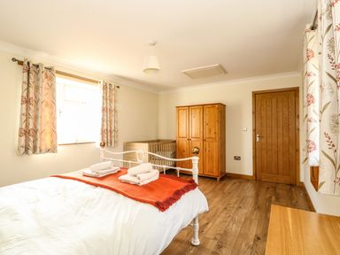 A bedroom with a double bed, wooden wardrobe, crib, wooden door, and floral curtains at Sunnyside Cottage in Blackborough End near King's Lynn