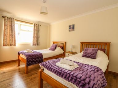 A bedroom with two single beds with purple throws and pillows a nightstand with a lamp and a window with curtains at Sunnyside Cottage in Blackborough End near King's Lynn