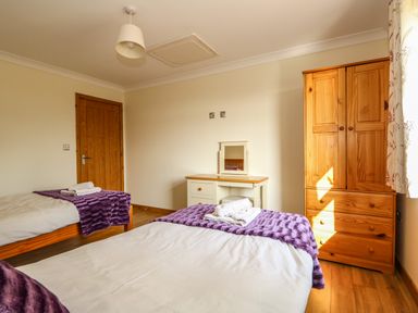 A bedroom with two single beds with purple blankets a wooden wardrobe and a white dressing table at Sunnyside Cottage in Blackborough End near Kings Lynn