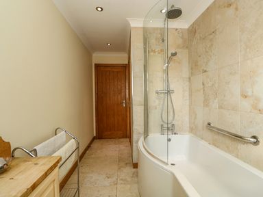 A bathroom with a bathtub and shower next to a wooden door at Sunnyside Cottage in Blackborough End near Kings Lynn