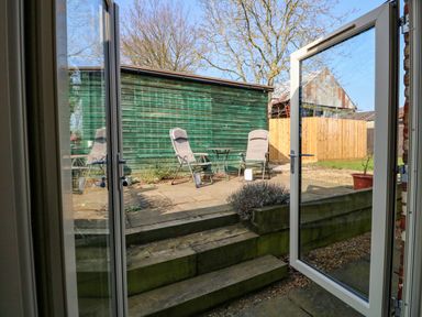 A patio with two chairs and a small table outside wooden steps and a green shed at Sunnyside Cottage in Blackborough End near King's Lynn