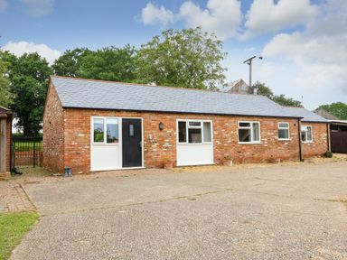 A single story brick building with several windows and a black door in a paved area at Sunnyside Cottage Blackborough End near Kings Lynn
