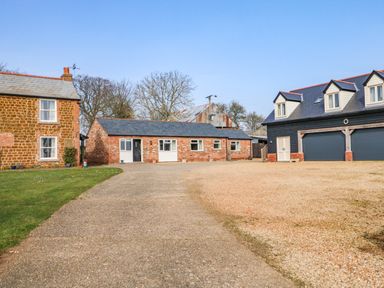 Driveway with gravel and paved sections in front of brick and black wooden buildings at Sunnyside Cottage in Blackborough End near Kings Lynn