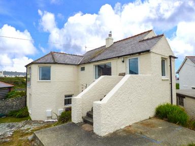 A two-story house with cream walls and slate roof with concrete steps leading to the entrance at Ty'r Enfys Bach - Upper in Trearddur Bay
