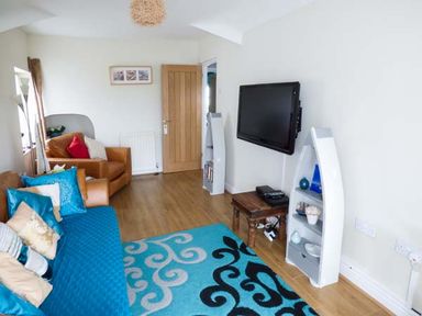A living room with a blue patterned rug a mounted flat screen tv and brown sofas at Tyr Enfys Bach - Upper in Trearddur Bay