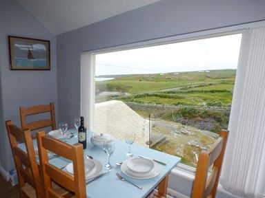 A dining table set for four with plates glasses and cutlery near a large window overlooking green fields at Ty'r Enfys Bach - Upper in Trearddur Bay