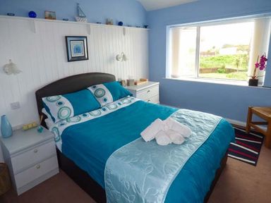 A bedroom with a double bed blue bedding bedside tables and a window with a view at Ty'r Enfys Bach - Upper in Trearddur Bay
