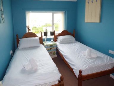 A bedroom with two single beds with white bedding and a small painted bedside table between them at Ty'r Enfys Bach - Upper in Trearddur Bay