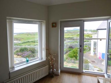 A corner of a room with a window and glass door overlooking a garden at Ty'r Enfys Bach - Upper in Trearddur Bay