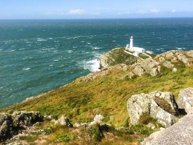 A rocky coastline with a lighthouse on a promontory overlooking the sea at Ty'r Enfys Bach - Upper in Trearddur Bay