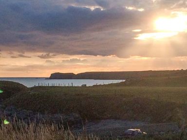 A coastal landscape with cliffs a grassy field and the ocean at Ty'r Enfys Bach - Upper in Trearddur Bay