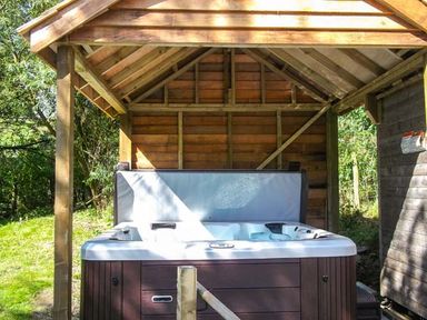 An outdoor hot tub under a wooden shelter in a garden at Ploony Cottage in Bleddfa